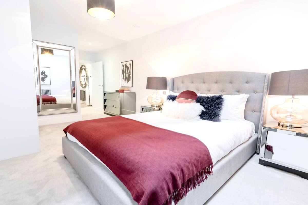 Une chambre moderne avec un grand lit, deux tables de chevet, un miroir et un plaid rouge.