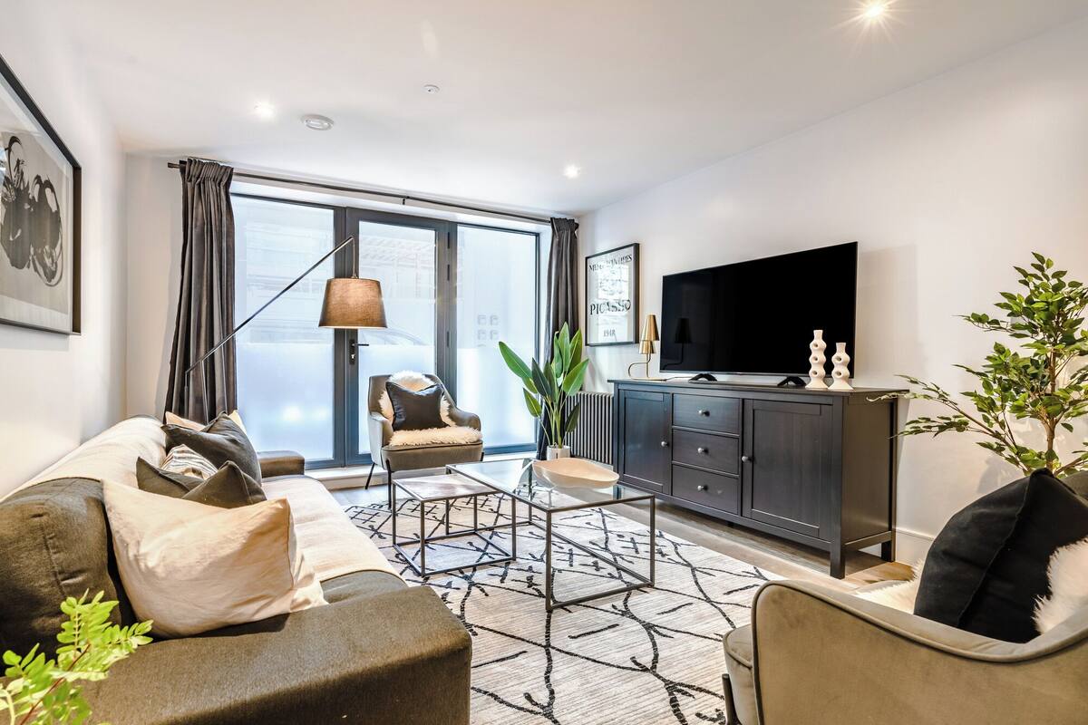 Un salon moderne avec un canapé, un fauteuil et un téléviseur posé sur un meuble.