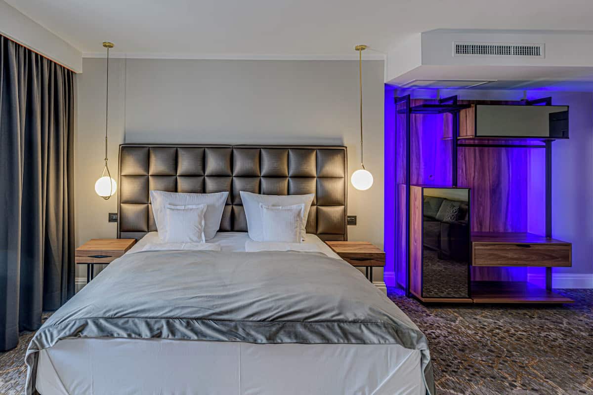 Una habitación de hotel con una cama grande, dos mesitas de noche, un espejo y una zona de estar con un banco.