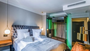 Ein Hotelzimmer mit einem bettbezogenen Kopfende, einem Nachttisch mit Lampe, einem Spiegel und Blick nach draußen durch eine Tür.