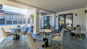 Ein Außenbereich mit runden Tischen und gepolsterten Stühlen, einem modernen architektonischen Design und Blick auf die Straße.