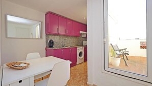 Una cocina compacta con armarios rosa, una lavadora y un comedor con una mesa y sillas blancas.