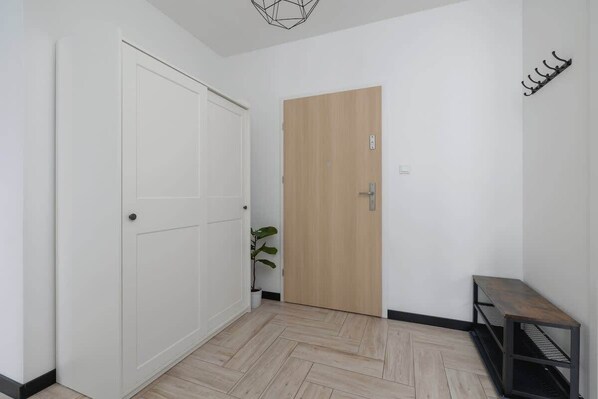 A hallway with a white door, a wooden door, a potted plant, and a bench.