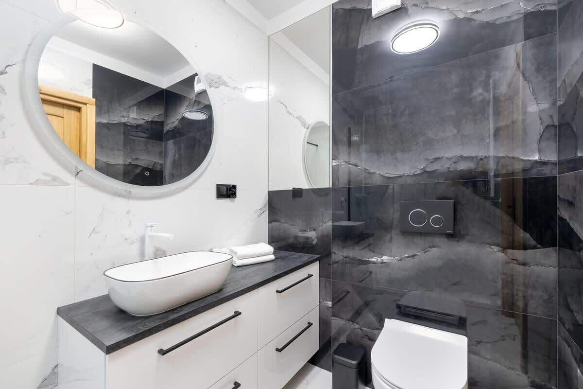 Een moderne badkamer met een witte wasbak, een ronde spiegel en een douchecabine met glazen wanden.