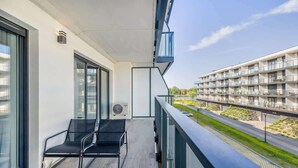 Un balcon avec deux chaises et une table, donnant sur une rue et d’autres immeubles.