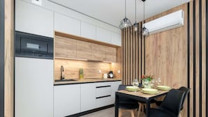 Une cuisine moderne avec des meubles blancs, un mur d’accent en bois et un coin repas comprenant une table et des chaises noires.