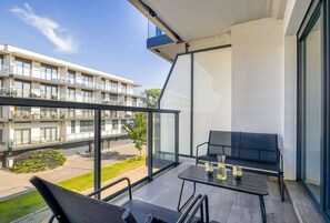 A balcony with a table and chairs, overlooking a building with multiple floors and a garden area.