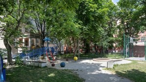 Un parque con juegos infantiles, una escalera azul y árboles.