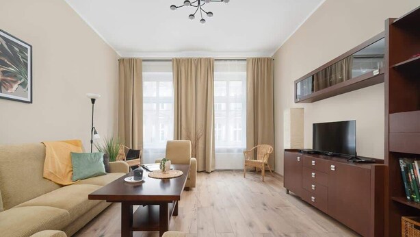 Una sala de estar con sofá, una mesa de centro, un televisor sobre un mueble bajo, y una zona de comedor con sillas.