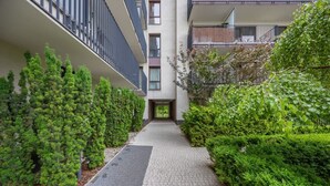 A narrow pathway flanked by neatly trimmed hedges and a modern building with balconies.