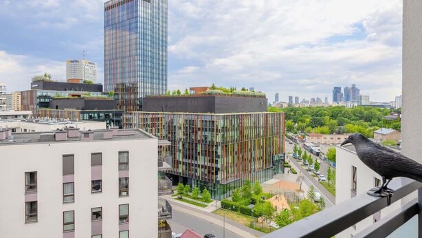 A modern building with a glass facade, surrounded by other structures and greenery.