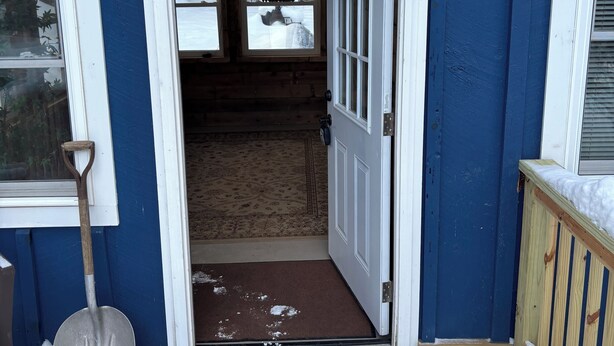 A wooden door leading to a covered porch with a snow-covered ground.