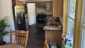 A compact kitchen with wooden cabinets, a stainless steel refrigerator, a built-in oven, and a window providing natural light.