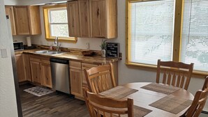 A modern kitchen with wooden cabinets, a dining table with chairs, a ceiling fan, and a window with blinds.