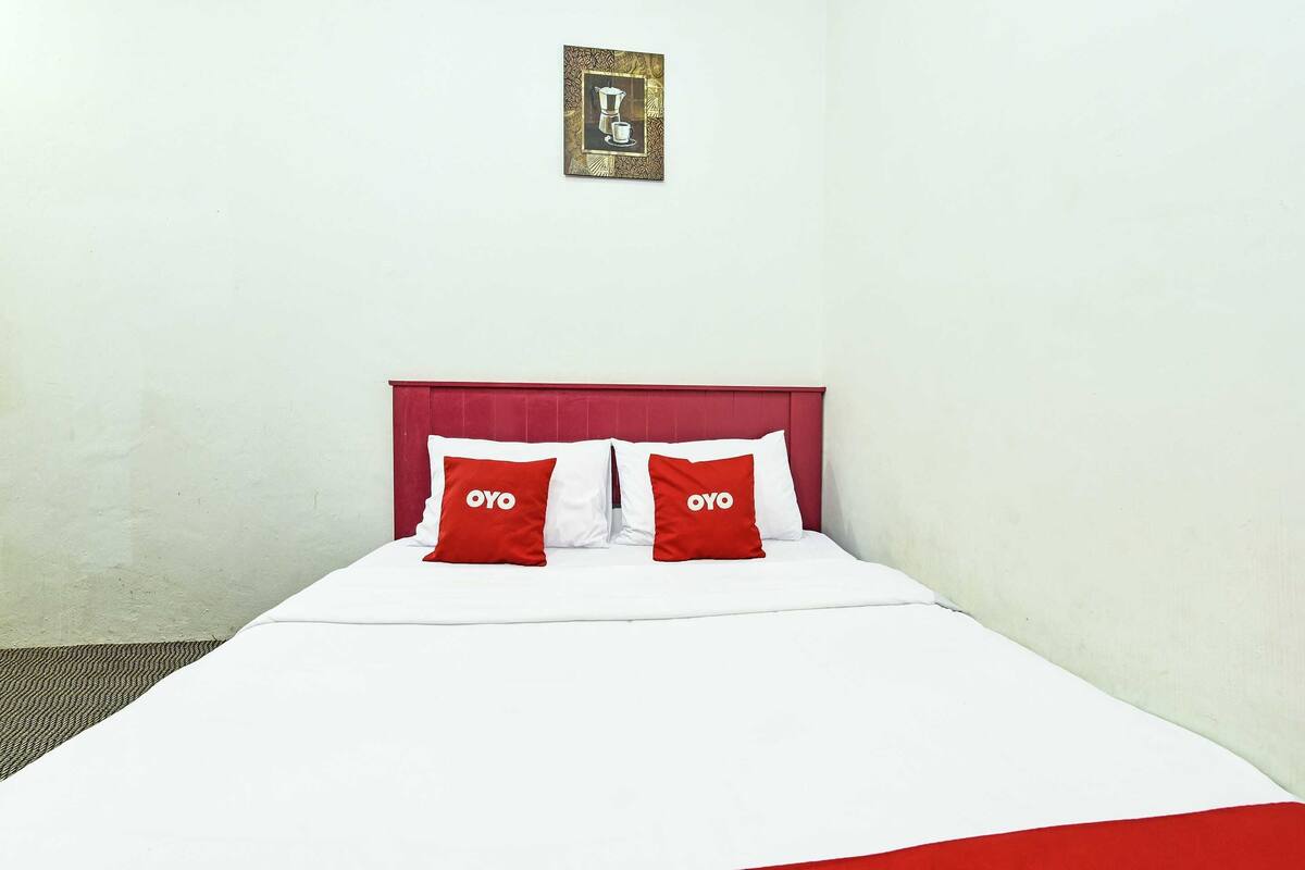 A single-bed room with a red headboard, white bedding, and two red pillows with the word "OYO" on them.