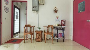 A hotel lobby with wooden chairs, a small table with a plant, a shelf with beverages, and a red door. - OYO 90999 DG HOTEL (Sungai Petani)