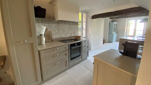 A modern kitchen with a built-in oven, a sink, and a countertop. There is a window providing natural light. - La Maison de la Bergère (Fox-Amphoux)