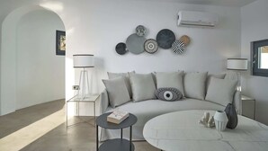 A modern living room with a sofa, a coffee table, and decorative plates on the wall. - Windmill superior with private plunge pool
 (FC2M+X3 Imerovigli, Greece)