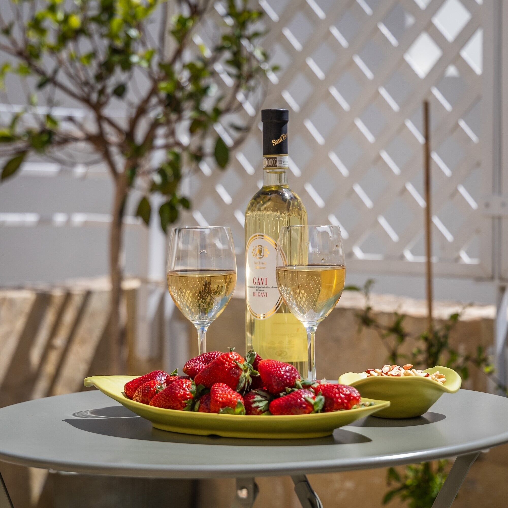A table with a bottle of white wine, two glasses, and a plate of strawberries.