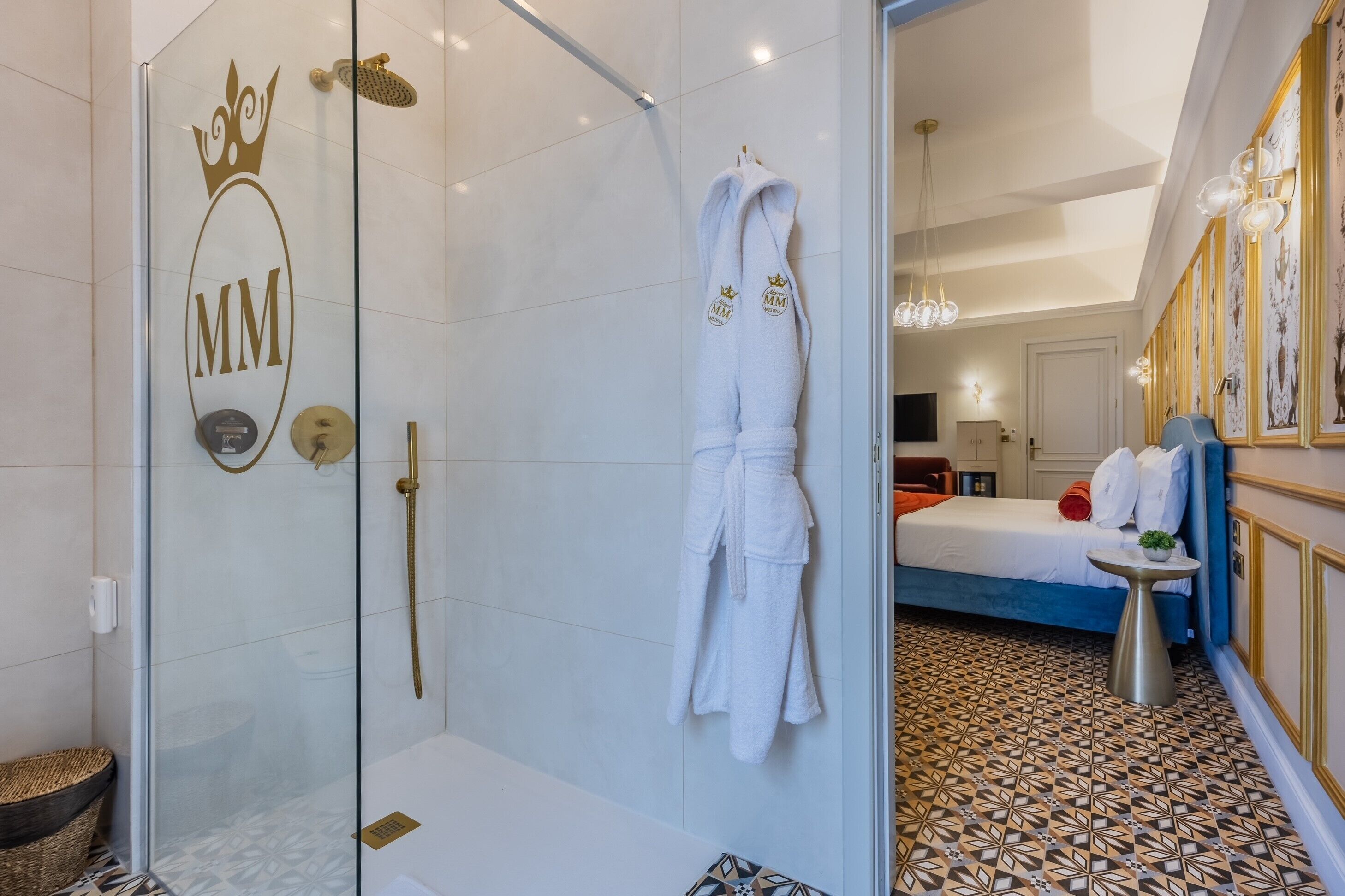 Une chambre d’hôtel avec une douche en verre, un lit avec un tapis à motifs et un peignoir orné d’un logo accroché au mur.