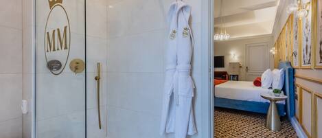 Une chambre d’hôtel avec une douche en verre, un lit avec un tapis à motifs et un peignoir orné d’un logo accroché au mur.