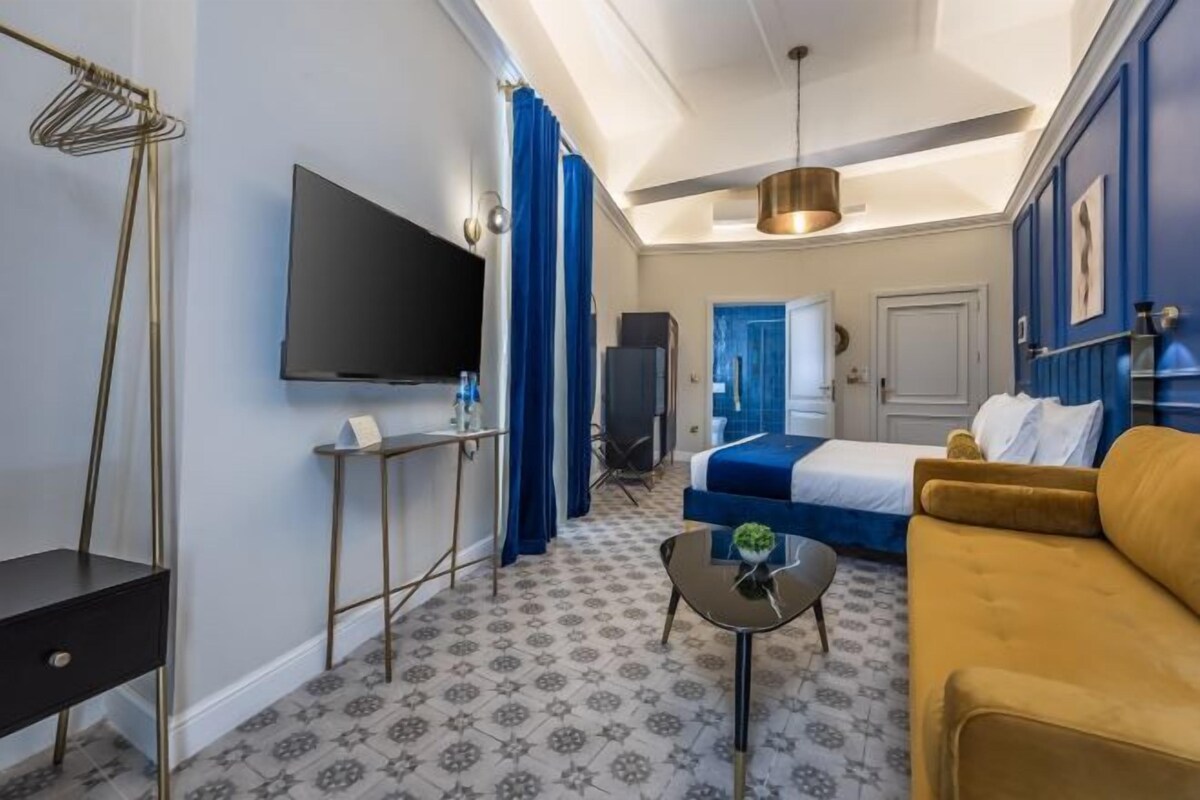 Una habitación de hotel con cama, sofá, televisión, una mesita y una lámpara en el techo.