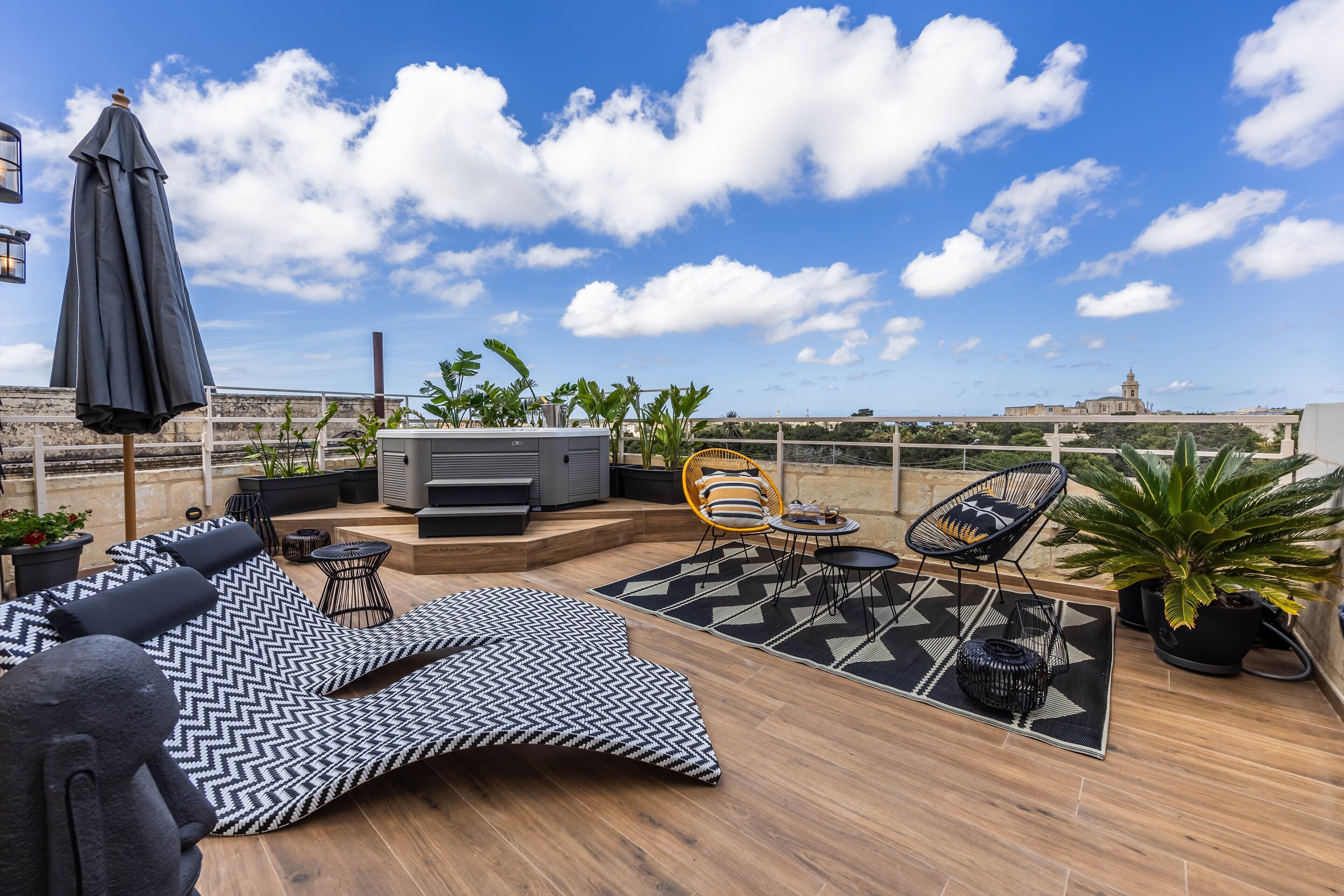 A rooftop terrace with a sofa, chairs, a table, and a large umbrella.