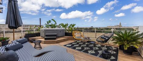 A rooftop terrace with a sofa, chairs, a table, and a large umbrella.