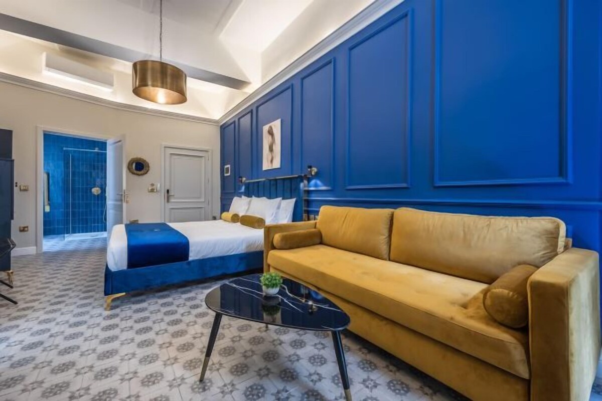 A hotel room with a bed, a sofa, a coffee table, and a blue accent wall.