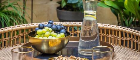 A wicker table with a bowl of fruit, a glass pitcher, and two glasses.