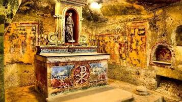 Eine Steinkapelle mit einer zentralen Statue, Mosaikverzierungen und einem Kreuzsymbol am Altar.