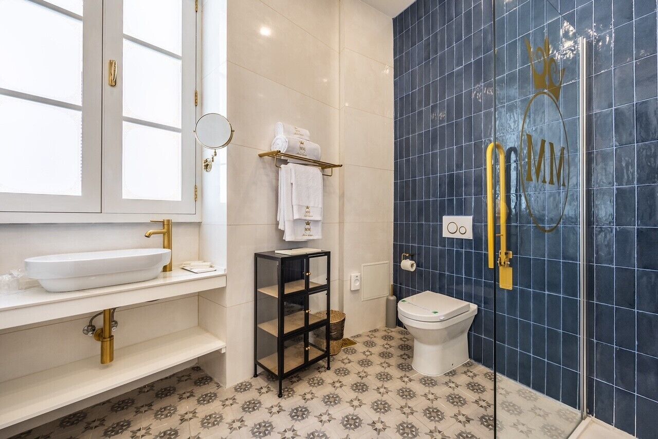 A bathroom with a white sink, a black shelf, a toilet, and blue tiled walls.