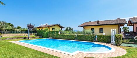 A rectangular swimming pool with a tiled edge, surrounded by a well-maintained lawn and a hedge.