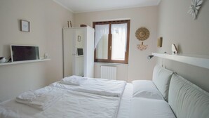 Une chambre à coucher comprenant un lit, une télévision, une armoire, une fenêtre avec des rideaux et un élément décoratif mural.