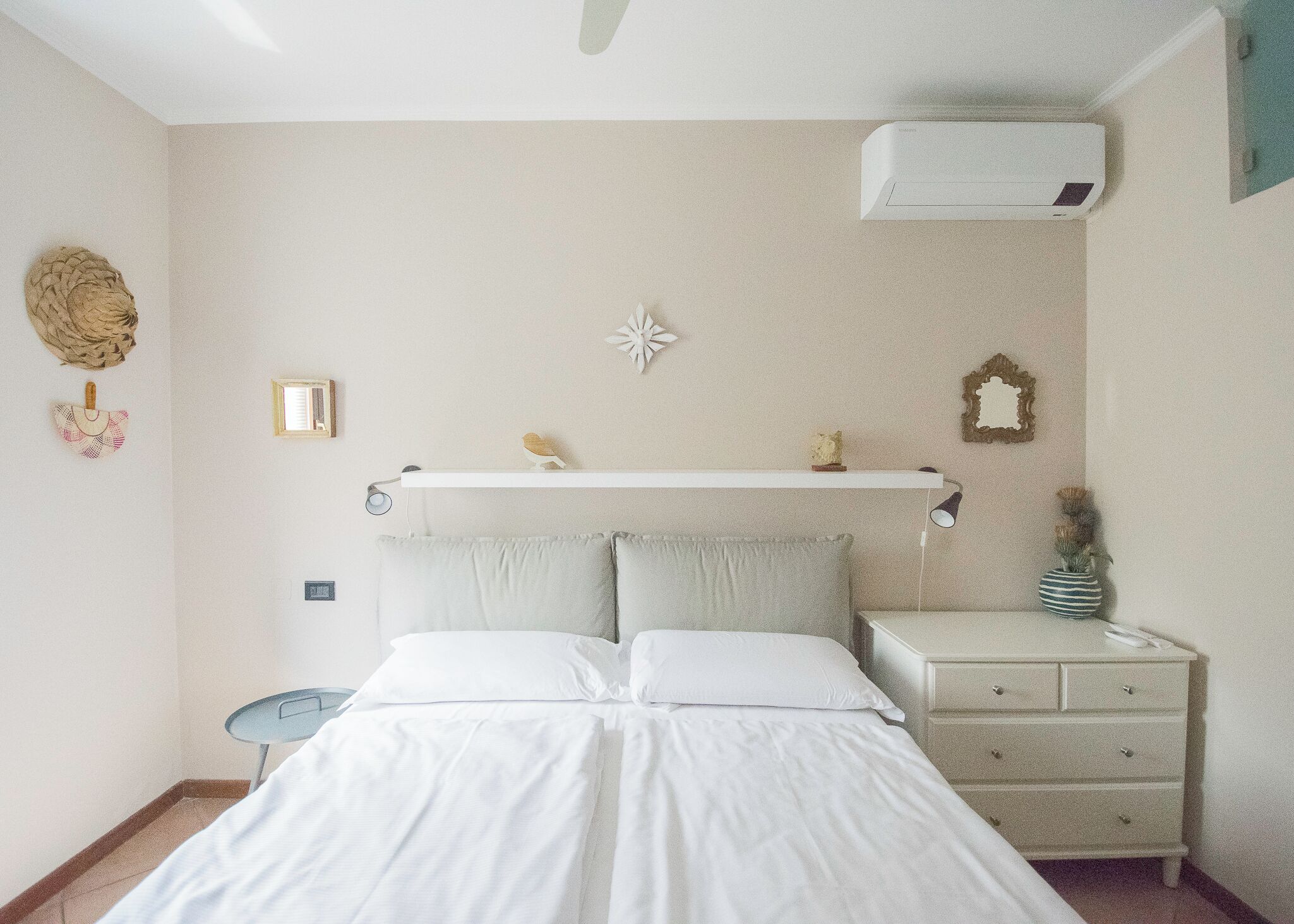 A bedroom with a bed, bedside tables, a wall-mounted shelf, and an air conditioning unit.
