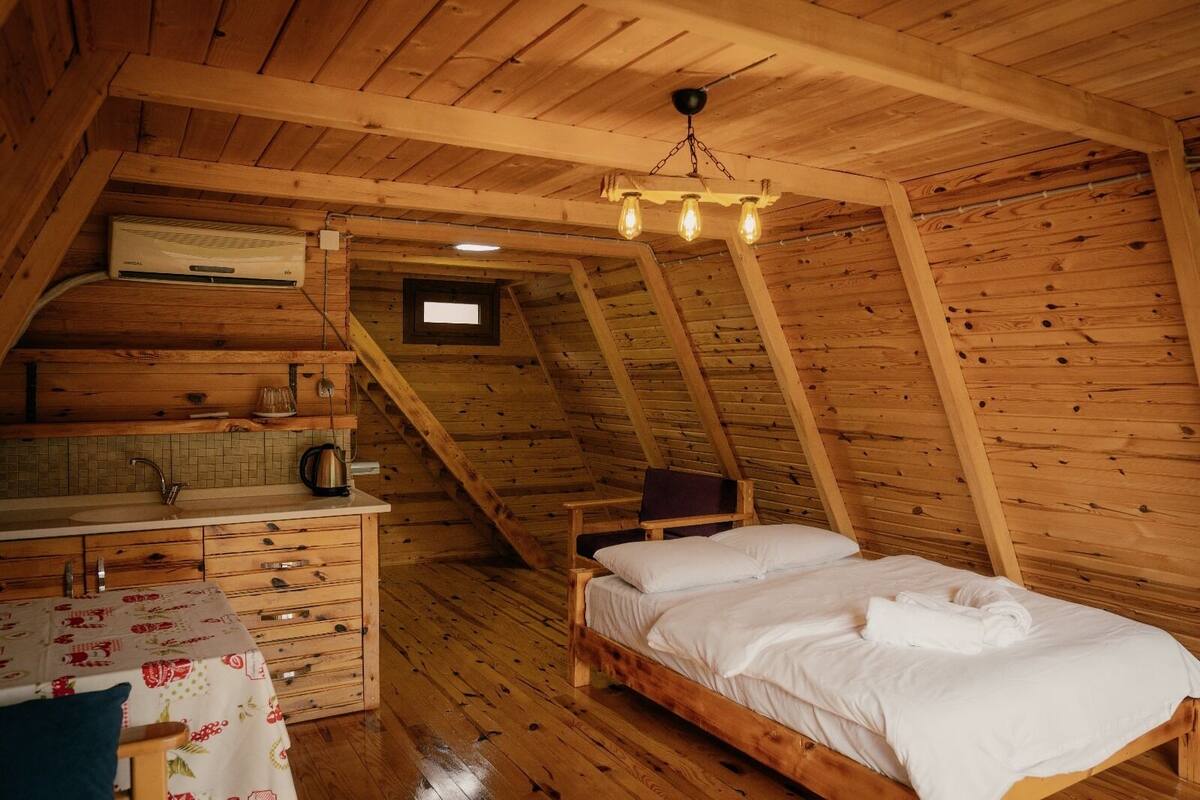 Une cabane en bois avec une chambre à coucher située en mezzanine, une petite cuisine et une petite fenêtre.