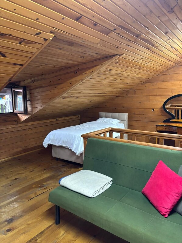 Une pièce mansardée chaleureuse, avec un canapé vert, un lit recouvert de linge de lit blanc et un plafond en bois.