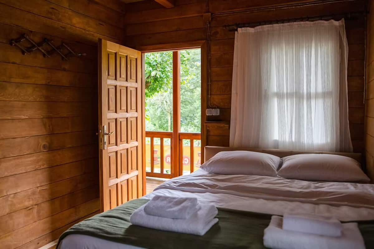 Une pièce de style cabane en bois, avec un lit, une porte donnant sur un espace extérieur et une fenêtre avec des rideaux.