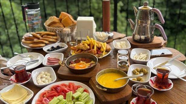 A table with various food items and a teapot on a wooden table outdoors. - Elagza Dag Evleri (Pazar)