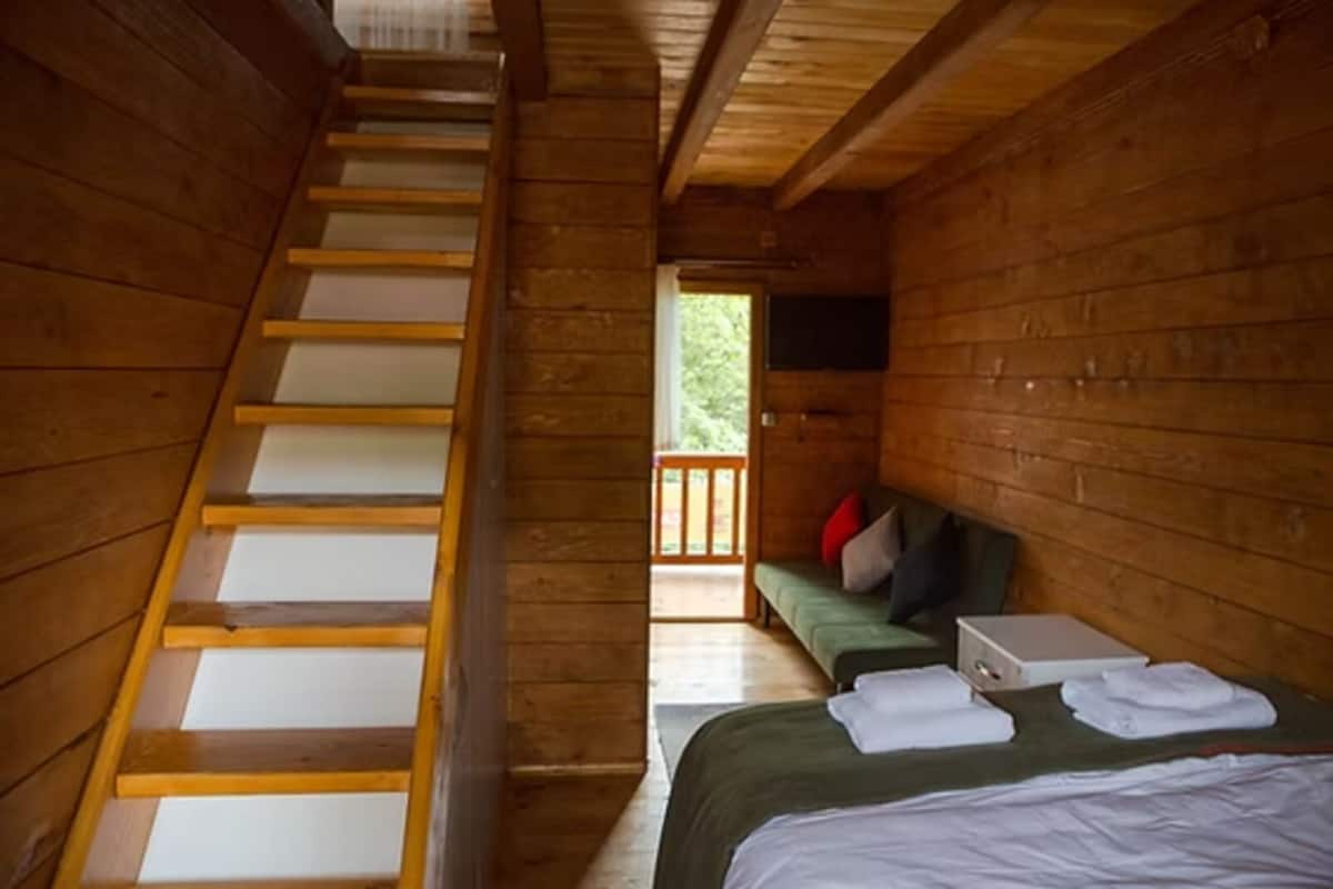 L’intérieur d’un chalet en bois comprend un escalier, un lit avec des oreillers, un banc et un téléviseur.