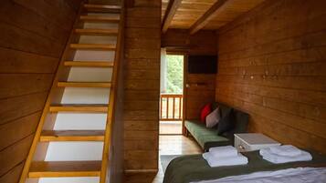 Interior de una cabaña de madera con una escalera, una cama con almohadas, un banco y un televisor.
