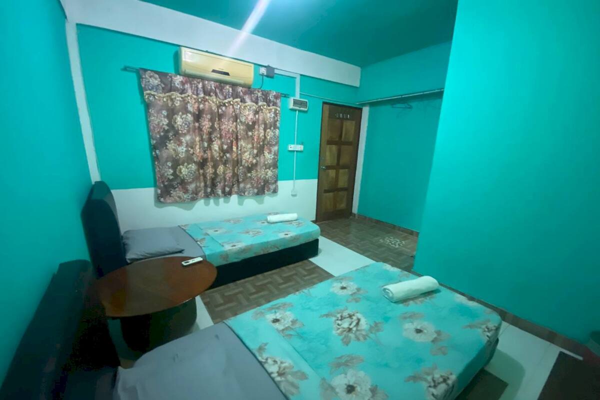 A room with teal walls, a bed with floral bedding, a small table, a chair, and a door.