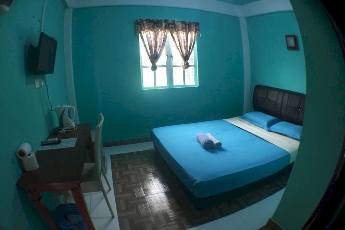 A room with a bed, a desk, a chair, a window with curtains, and a television on the wall.