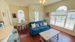 A living room with a blue sofa, white coffee table, and a dining area with a white table and chairs. - Lovely 1BR condo in Myrtlewood (Myrtle Beach)