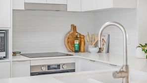 A modern kitchen with white cabinetry, a built-in stove, a digital clock, and a wooden cutting board.