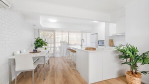Een moderne keuken met witte kastjes, een centraal eiland, barkrukken en een potplant.