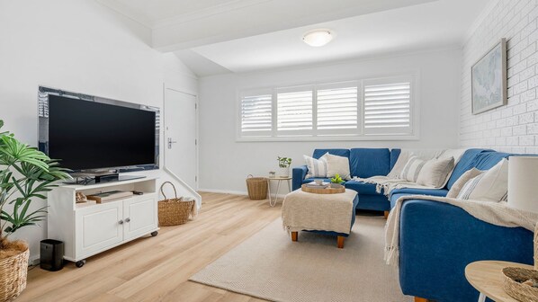 A living room with a television, sofa, and a large window with blinds.