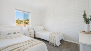 Een slaapkamer met twee bedden, een raam met uitzicht en een witte bakstenen muur.