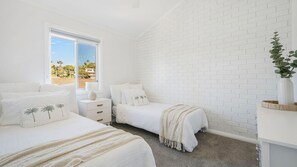 Quarto com duas camas, janela com vista e parede de tijolos brancos.