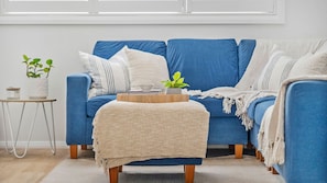 A blue sofa with a woven throw blanket, a small wooden side table with a plant, and a white vase.
